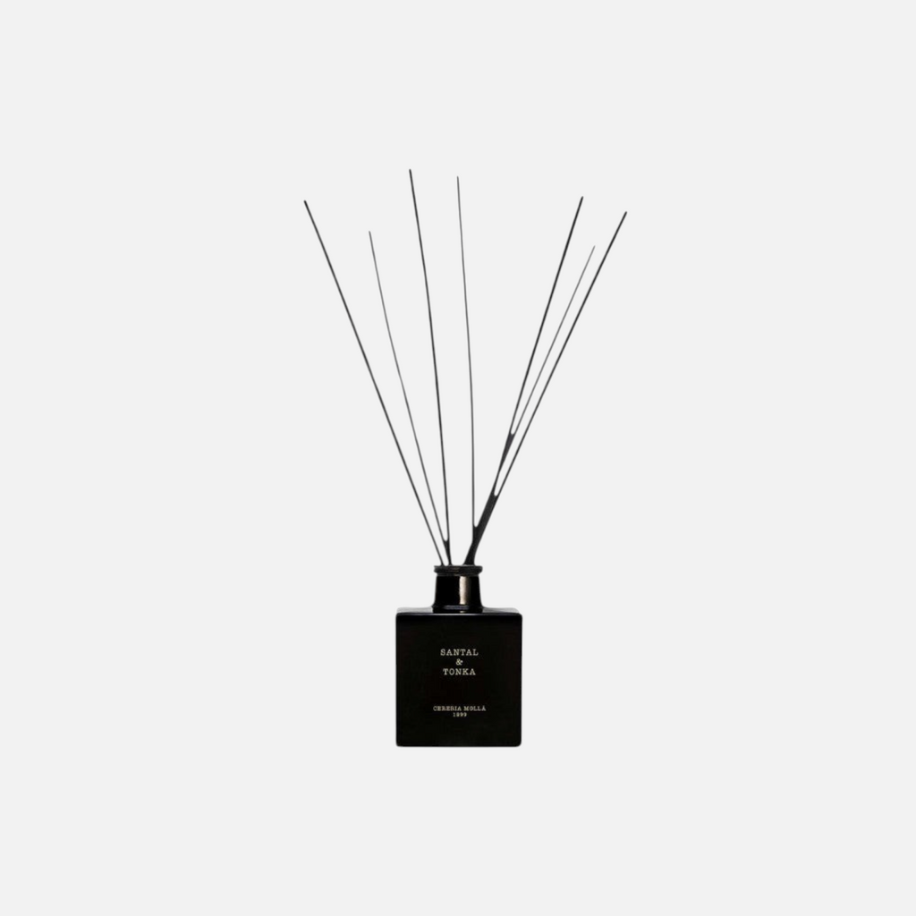 Citrine Home Santal & Tonka diffuser in a black glass bottle with black reed sticks against a light grey background.