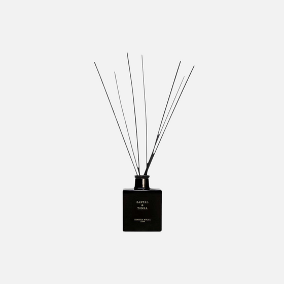 Citrine Home Santal & Tonka diffuser in a black glass bottle with black reed sticks against a light grey background.