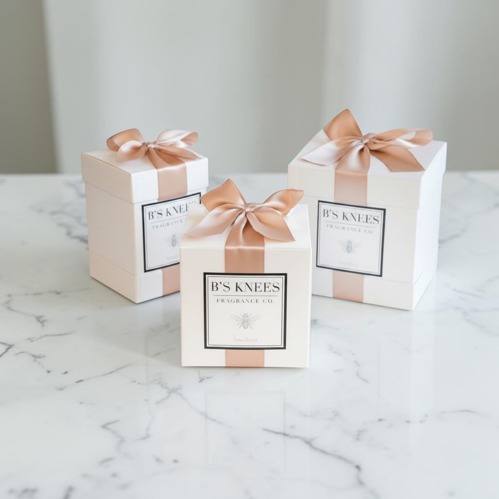 Three Citrine Home Basilica scented candle gift boxes in white with elegant satin ribbon bows on a marble surface.