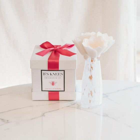 Citrine Home Essence of Holiday diffuser with white flower reed in a glass vase next to a gift box with red ribbon.