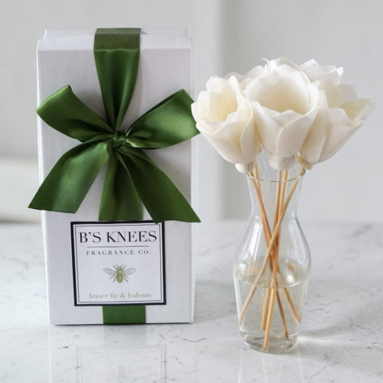 Citrine Home Fraser Fir & Balsam diffuser with white flower reeds in a glass vase next to a gift box with a green bow