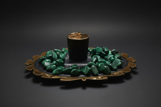 Citrine Home Malachite candle in a black vessel surrounded by green malachite stones on an ornate brass tray