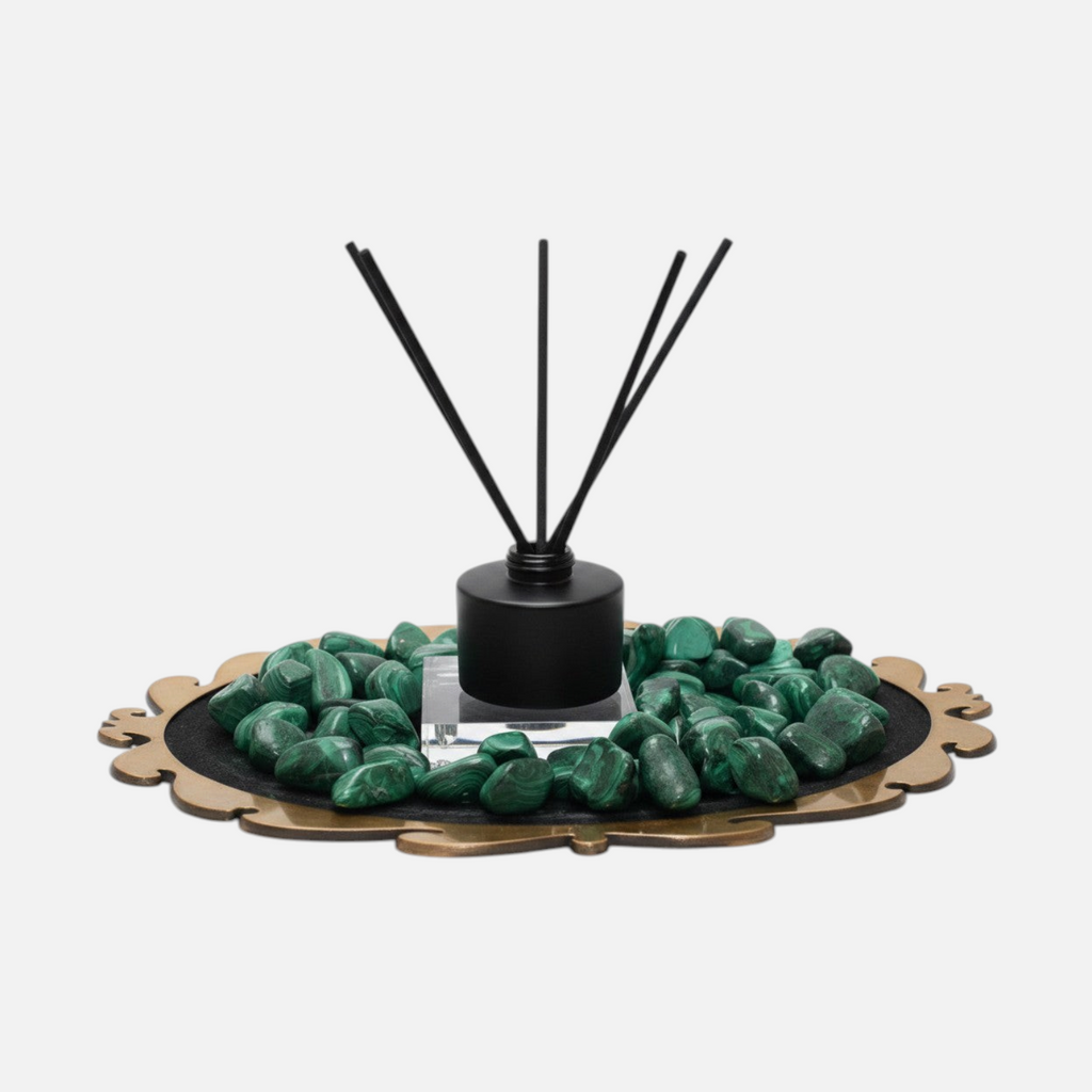 Citrine Home Malachite reed diffuser with black bottle and sticks, surrounded by green malachite stones on a tray.