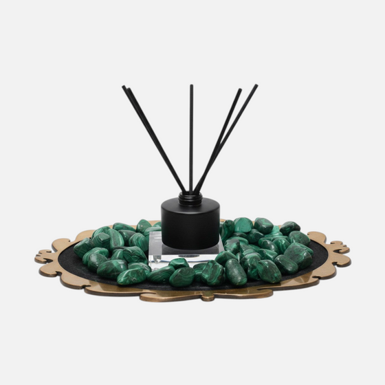 Citrine Home Malachite reed diffuser with black bottle and sticks, surrounded by green malachite stones on a tray.