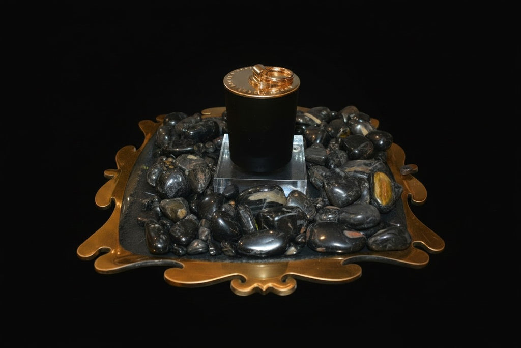 Citrine Home Onyx candle in a black vessel, displayed on a decorative gold tray surrounded by polished black stones.