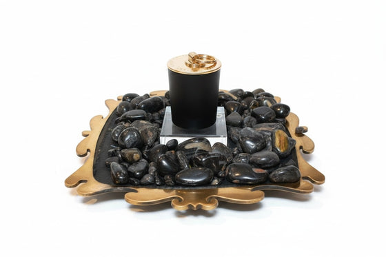 Citrine Home Onyx candle in a black vessel with a gold lid, displayed on a decorative tray with black river stones.