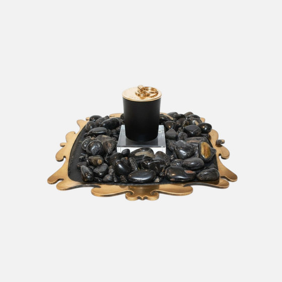 Citrine Home Onyx candle in a black vessel with a gold lid, displayed on a decorative tray with black river stones.