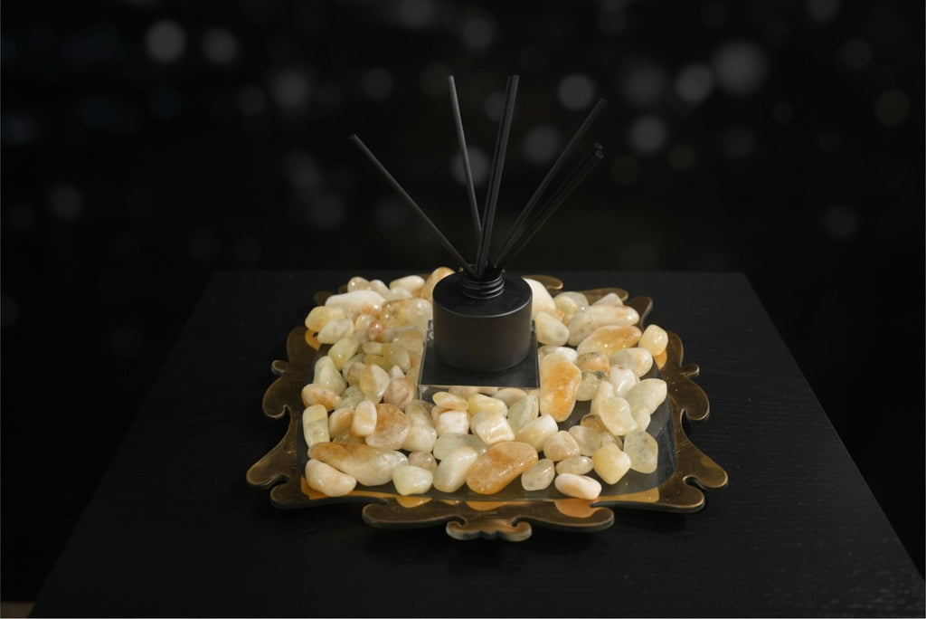 Citrine Home reed diffuser with black reeds, set on a decorative tray filled with polished citrine stones.