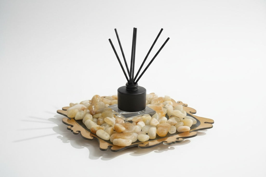 Citrine Home reed diffuser with black reeds, set on a decorative tray filled with smooth polished citrine stones.