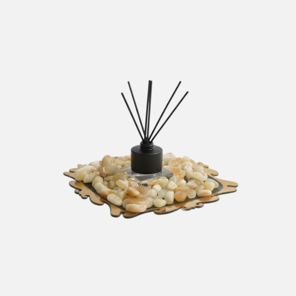 Citrine Home reed diffuser with black reeds, set on a decorative tray filled with smooth polished citrine stones.