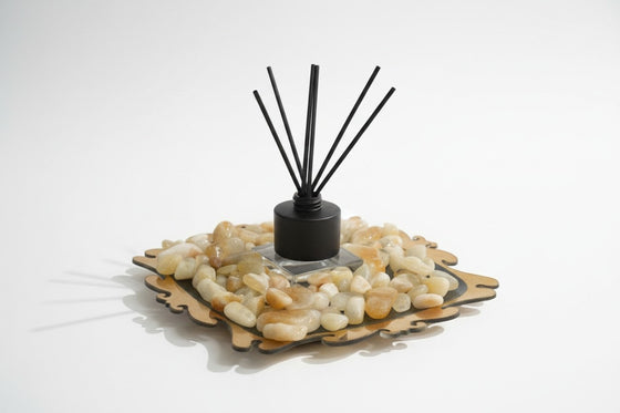 Citrine Home reed diffuser with black reeds, set on a decorative tray filled with smooth polished citrine stones.