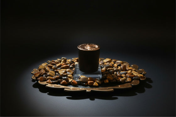 Citrine Home Tiger's Eye candle in a black vessel surrounded by polished tiger's eye stones on a decorative bronze tray