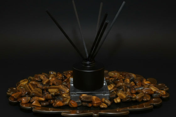 Citrine Home Tiger's Eye reed diffuser with black reeds, set on a decorative tray filled with polished tiger's eye stones.