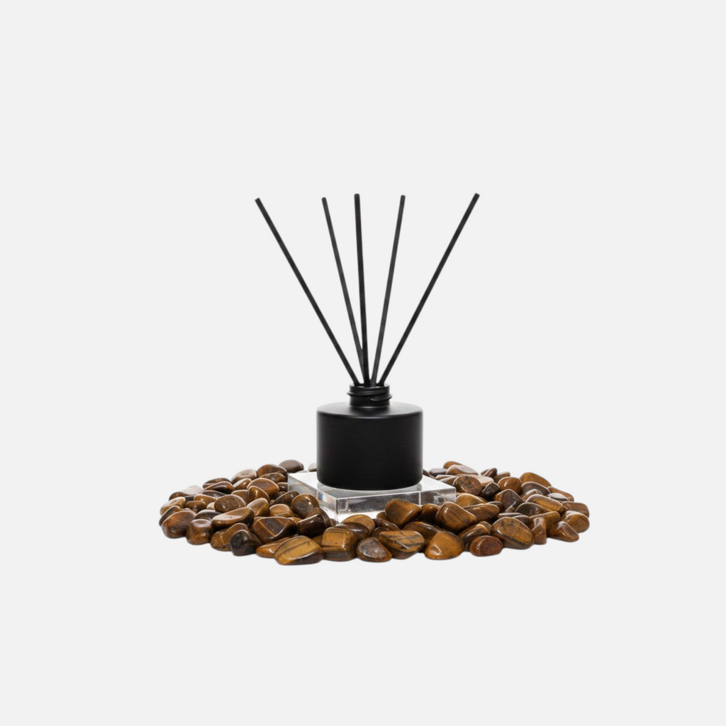 Citrine Home Tiger's Eye reed diffuser with black bottle and reeds surrounded by polished tiger's eye stones.