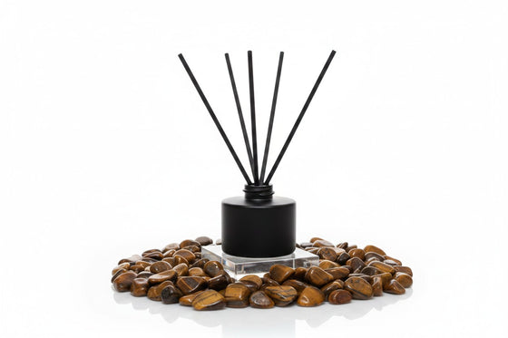 Citrine Home Tiger's Eye reed diffuser with black bottle and reeds surrounded by polished tiger's eye stones.