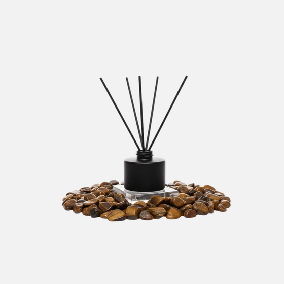 Citrine Home Tiger's Eye reed diffuser with black bottle and reeds surrounded by polished tiger's eye stones.