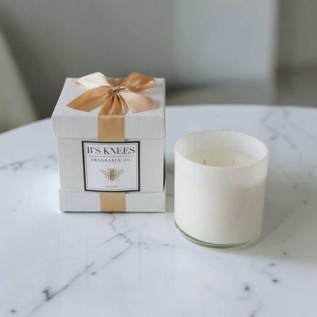 Citrine Home Veneto white scented candle in a glass jar next to a gift box with a gold ribbon on a marble table.