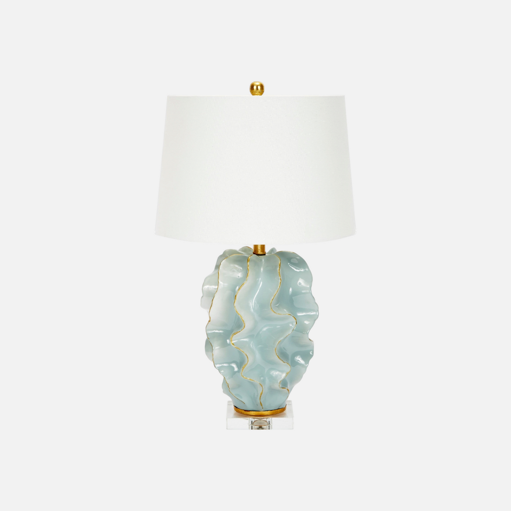 Citrine Home Hannah ceramic wave table lamp in blue with gold trim and a white linen drum shade on a clear base.