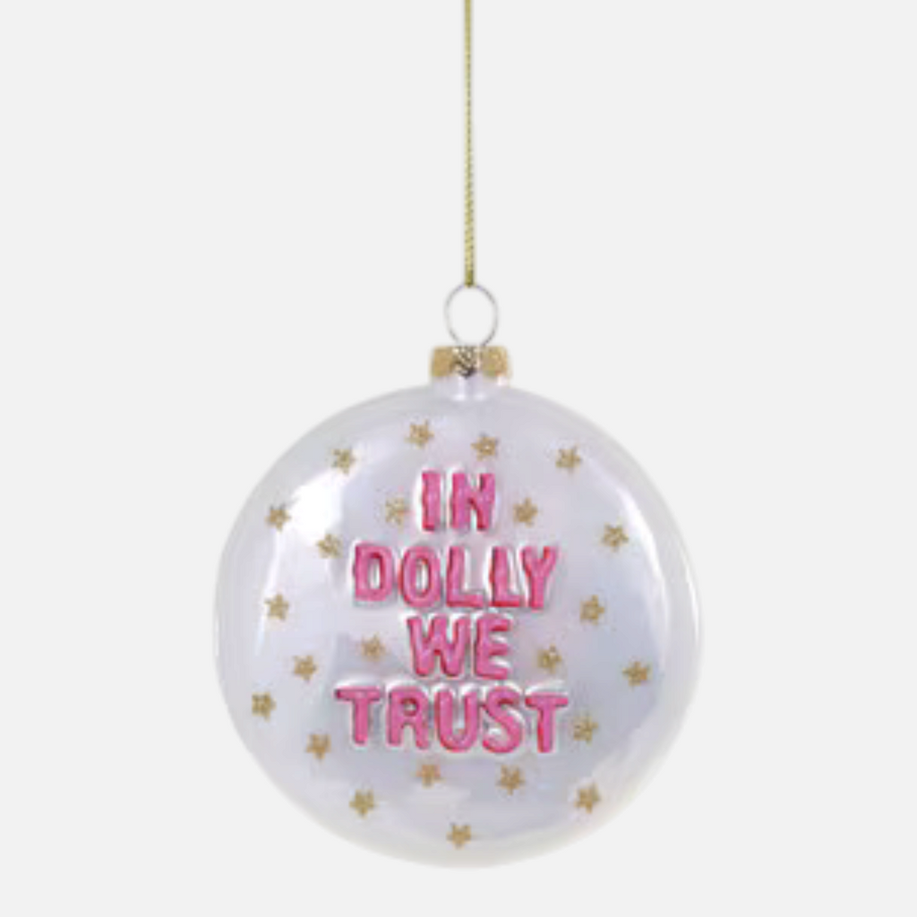 Citrine Home glass ornament featuring pink In Dolly We Trust text and gold star accents on a clear round bauble